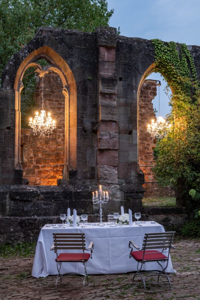 Romantische Hochzeitskulisse in der Klosterruine des Hotel Kloster Hornbach mit Kronleuchter und festlich gedecktem Tisch im Innenhof.
