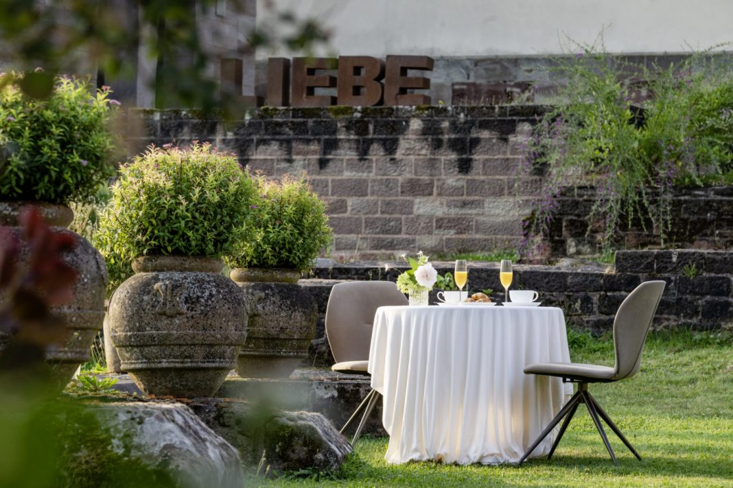 Hochzeitsempfang im Klostergarten des Hotel Kloster Hornbach mit gedecktem Tisch, Sektgläsern und Blick auf historische Klostermauern und den Schriftzug 