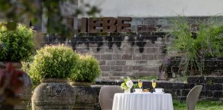 Hochzeitsempfang im Klostergarten des Hotel Kloster Hornbach mit gedecktem Tisch, Sektgläsern und Blick auf historische Klostermauern und den Schriftzug "Liebe" in übergroßen Lettern..