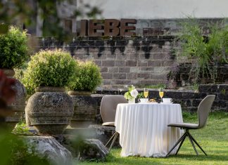 Hochzeitsempfang im Klostergarten des Hotel Kloster Hornbach mit gedecktem Tisch, Sektgläsern und Blick auf historische Klostermauern und den Schriftzug "Liebe" in übergroßen Lettern..