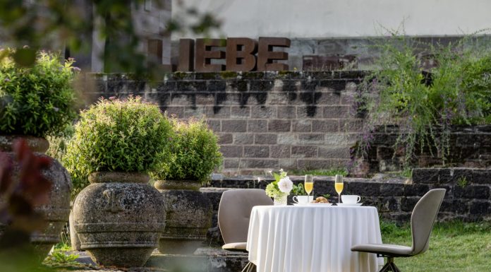 Hochzeitsempfang im Klostergarten des Hotel Kloster Hornbach mit gedecktem Tisch, Sektgläsern und Blick auf historische Klostermauern und den Schriftzug "Liebe" in übergroßen Lettern..