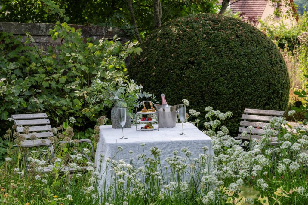 Sektempfang im Klostergarten des Hotel Kloster Hornbach mit festlich gedecktem Tisch im grünen Kräutergarten und historischer Gartenkulisse.
